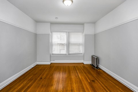 A room with wooden floors and a window with blinds.