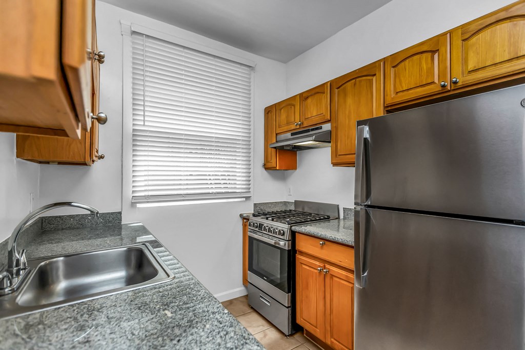 A kitchen with a stainless steel refrigerator, sink, and wooden cabinets.