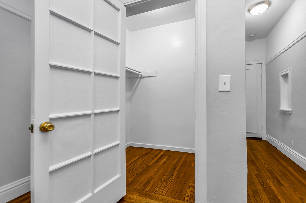 A white door with a gold handle is open to a hallway with wood floors.