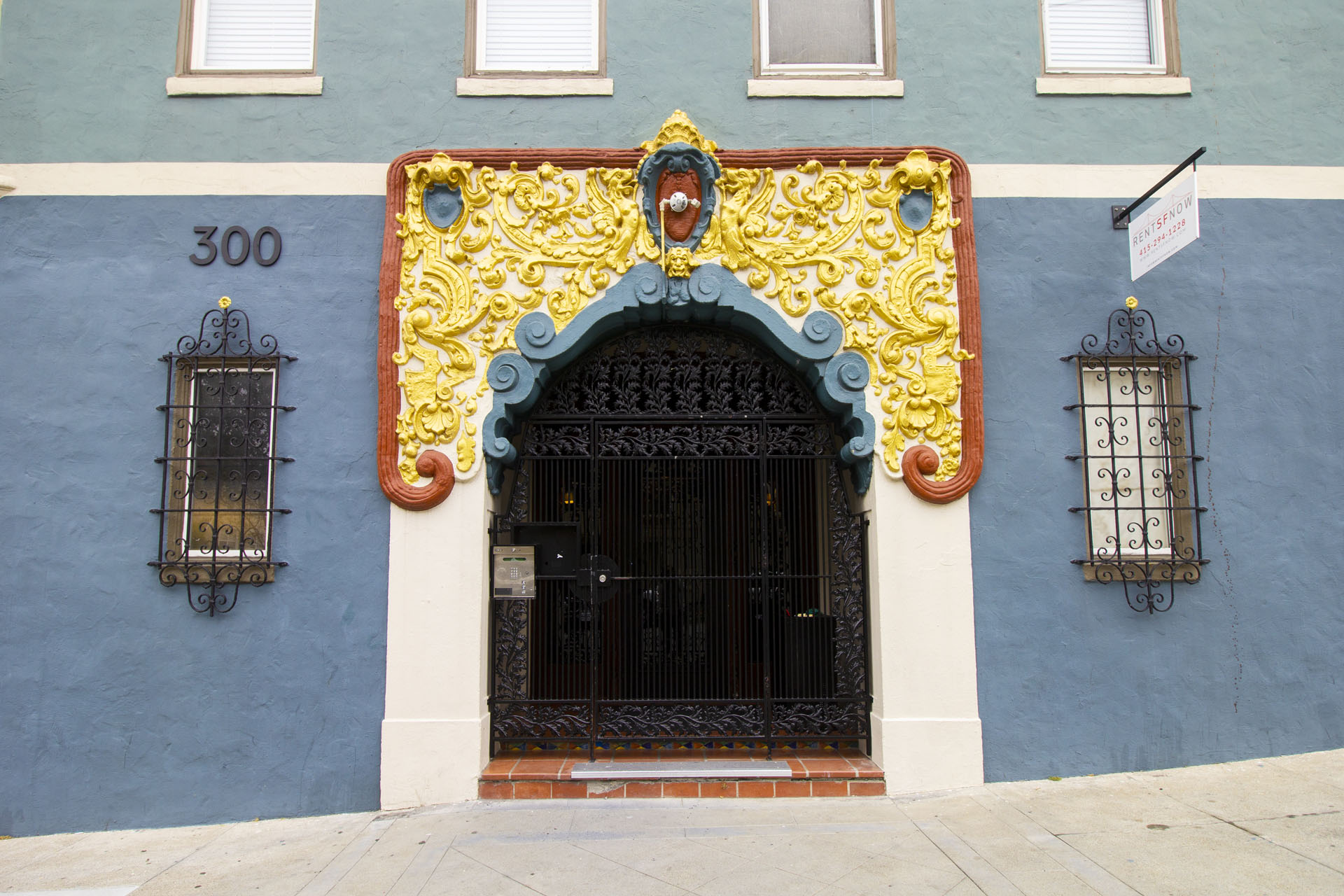 A blue building with a black door and a yellow decorative arch above it.