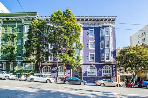 A row of colorful buildings with cars parked in front.