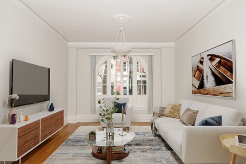 A living room with a white couch, a wooden coffee table, and a large window with a view of a city.