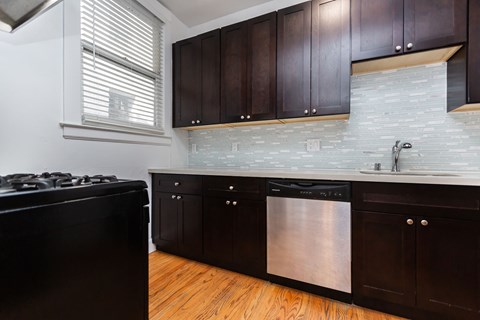 A kitchen with dark wood cabinets and a stainless steel dishwasher.