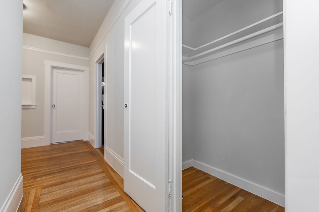 a bedroom with white walls and wood floors and a closet