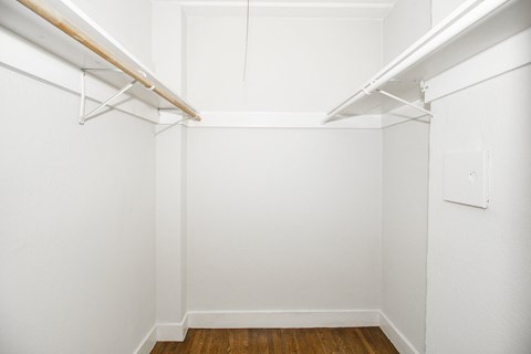 A white closet with a wooden shelf and a white door.