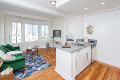 A living room with a green couch and a kitchen area in the background.