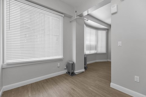A room with a window covered by white blinds and a radiator on the floor.