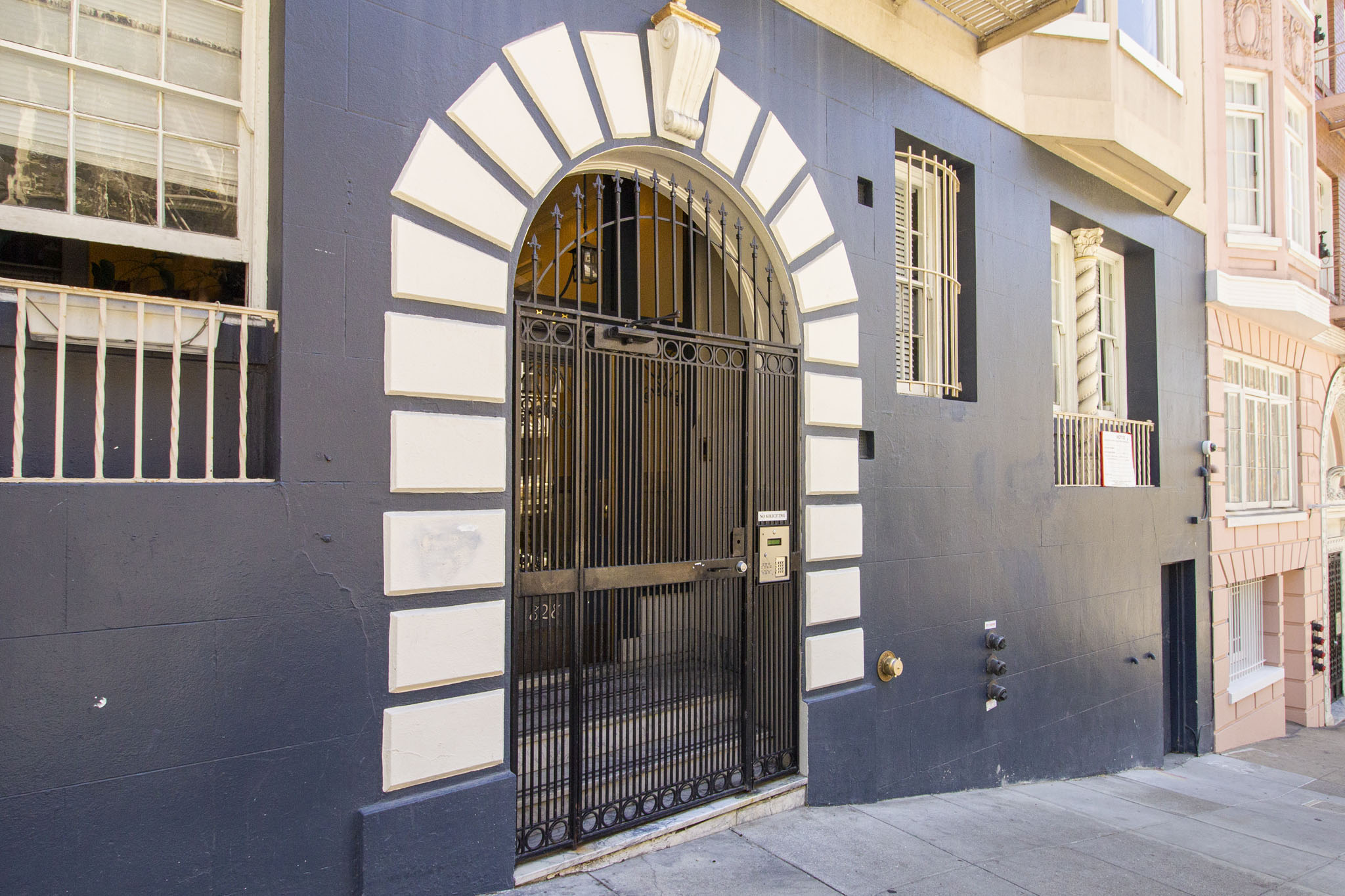 A black gate with a gold handle is in the middle of a white arch.