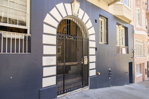 A black gate with a gold handle is in the middle of a white arch.