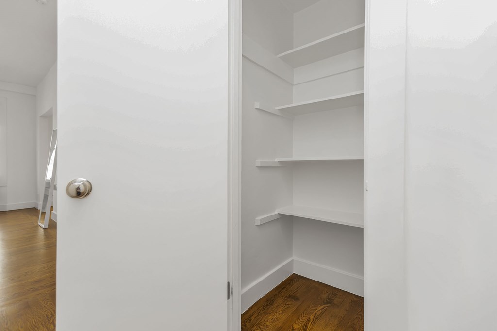 A white door with a silver handle is open to a hallway with white walls and wooden floors.
