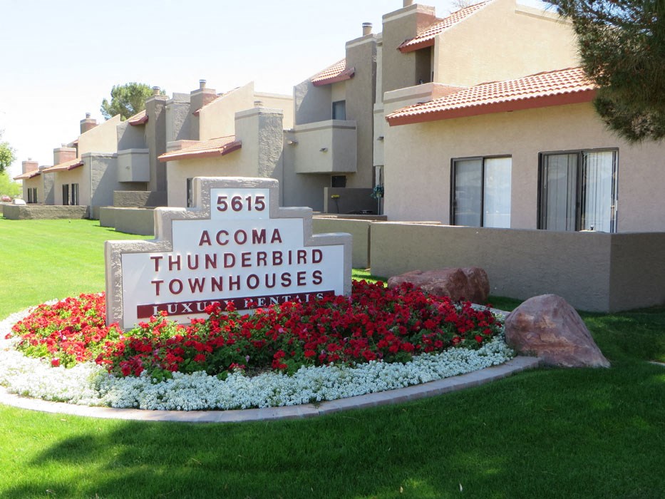 a round sign in front of a building with flowers and rocks