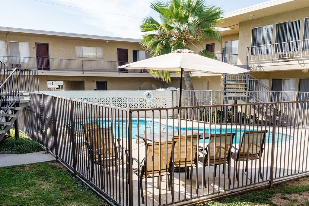 A pool surrounded by a black fence with chairs and an umbrella.