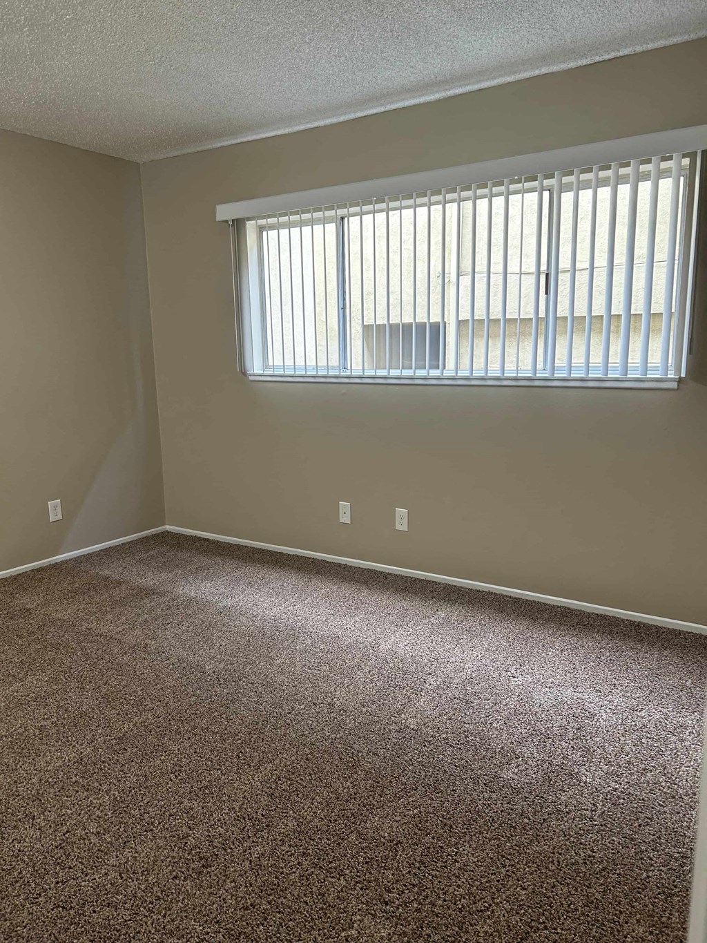 A room with a carpeted floor and a window with blinds.