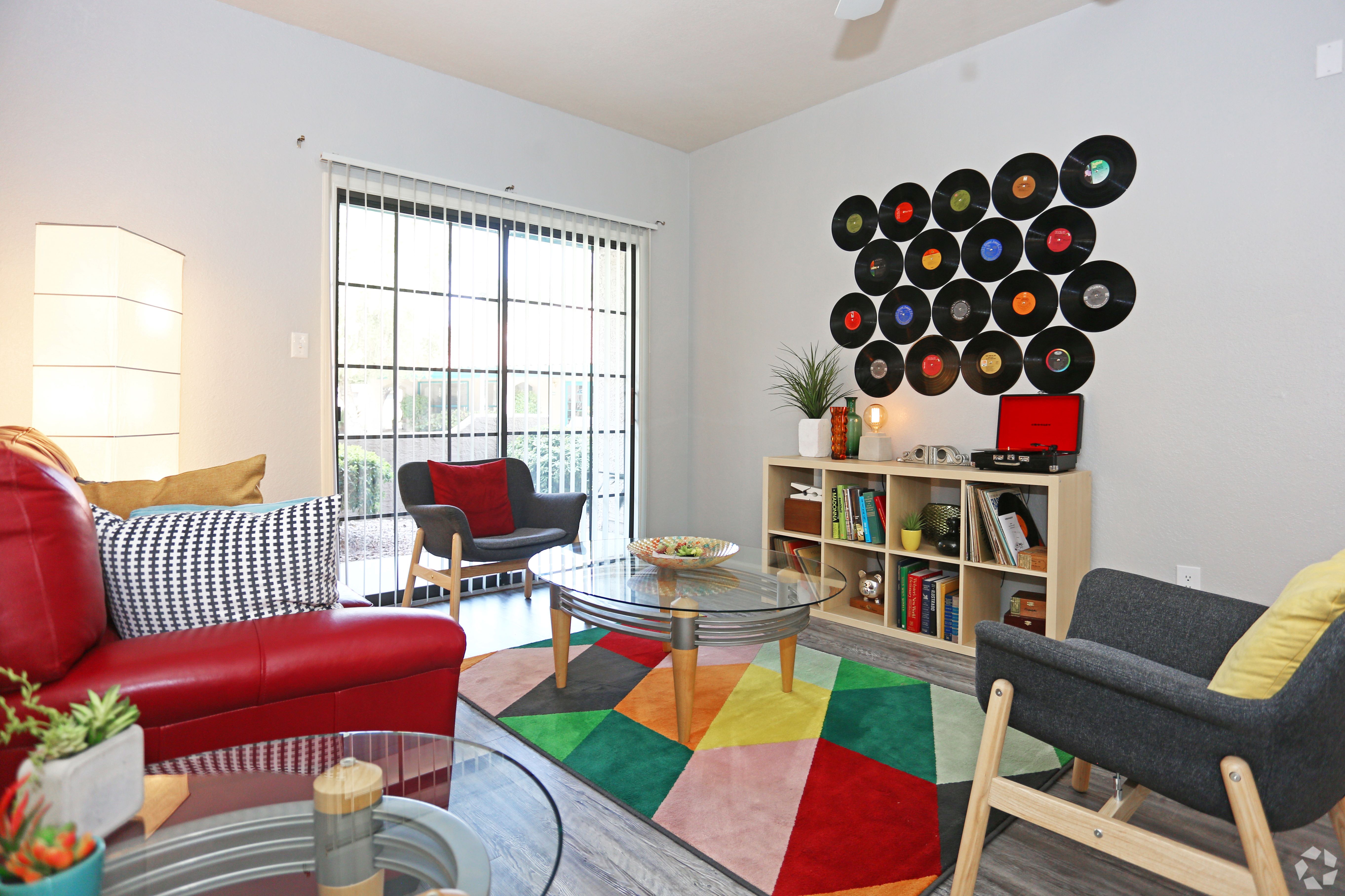 A living room with a red couch, a glass table, and a bookshelf with records on it.