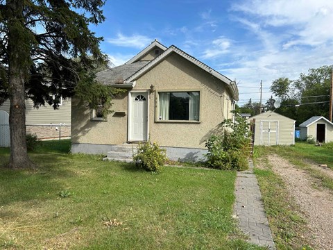 a small tan house with a sidewalk in front of it