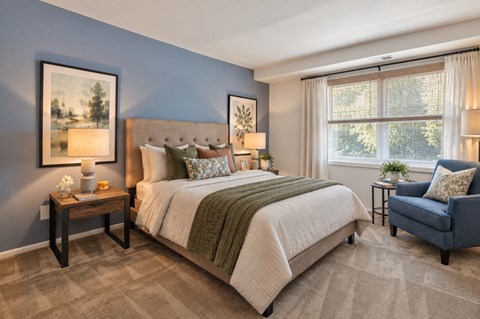 A bedroom with a large bed, a chair, and two framed pictures on the wall.