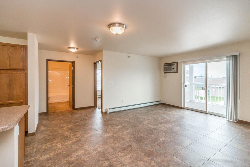 an empty living room with a kitchen and a sliding glass door