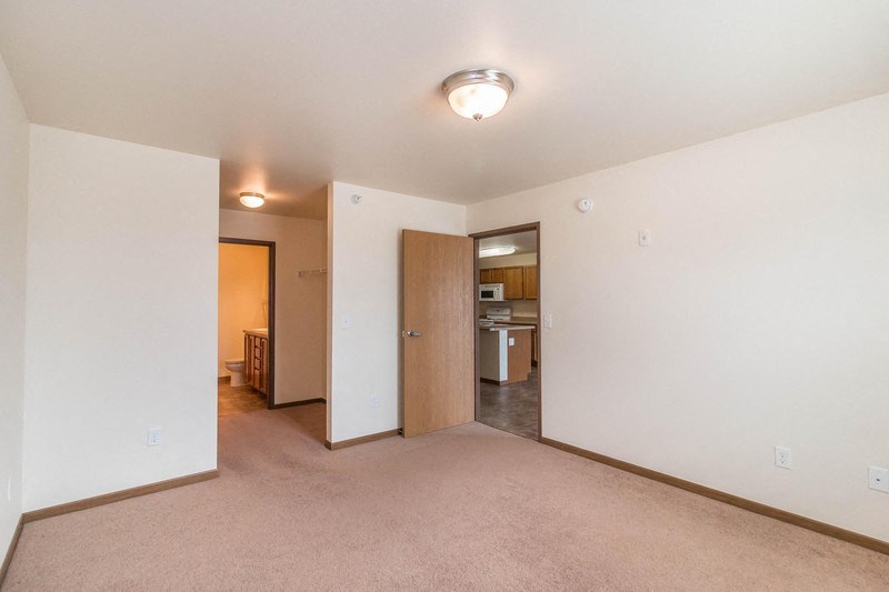 an empty living room with an open door to a kitchen