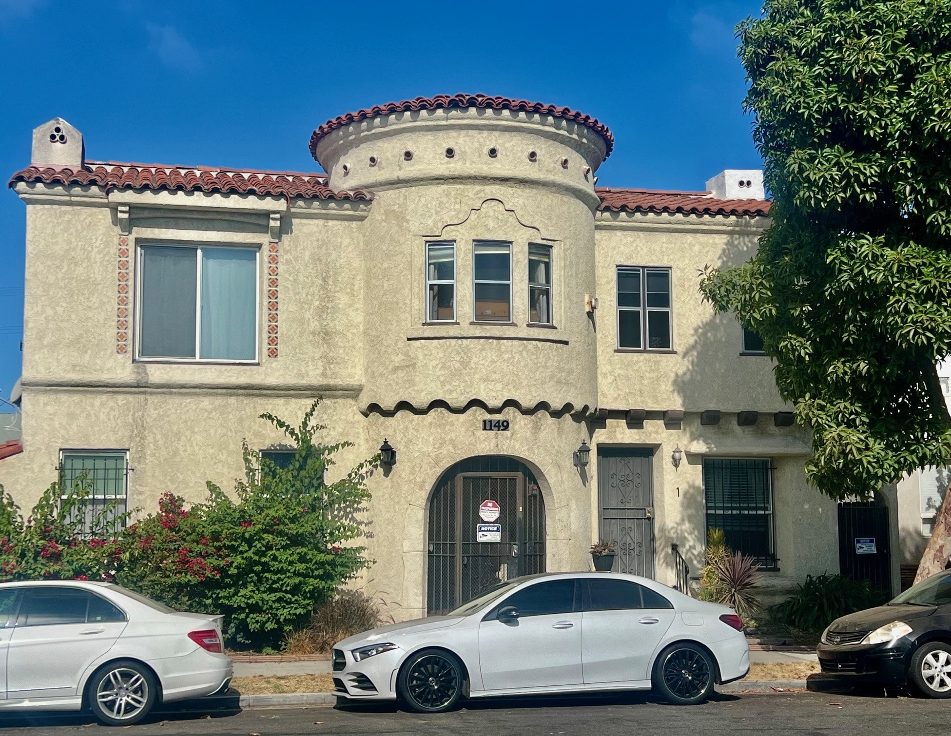 A white car is parked in front of a house with a red tile roof.
