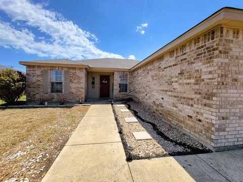 the front of a brick house with a sidewalk and grass