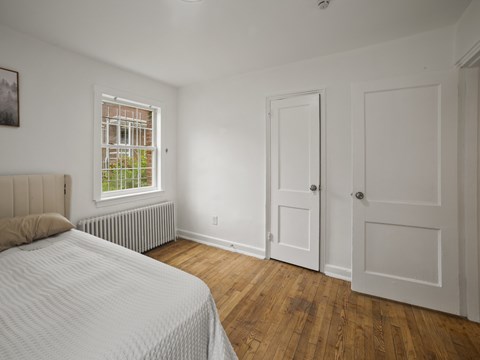 A bedroom with a bed, a window with a view of a garden, and a wooden floor.