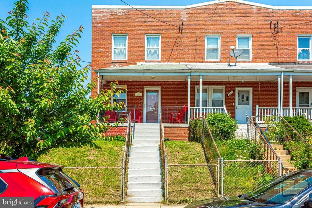 A red car is parked in front of a brick house.