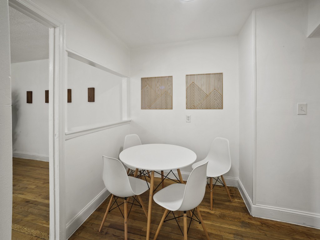 A white table with four chairs is in a room with white walls and wood floors.