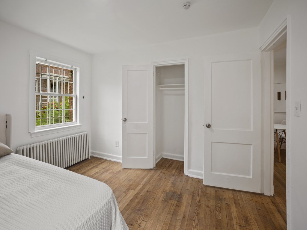 A white bedroom with a bed, wooden floors, and a window with bars.