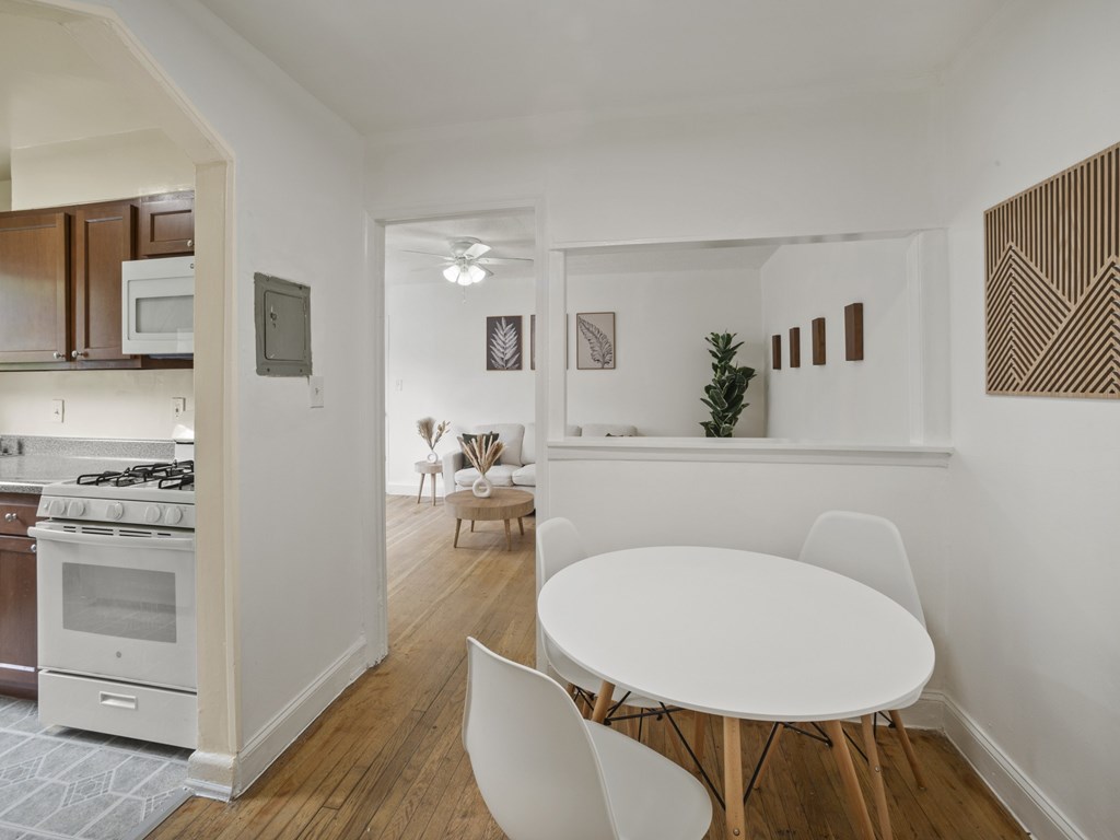 A white dining table with four chairs is in a room with white walls and wooden floors.