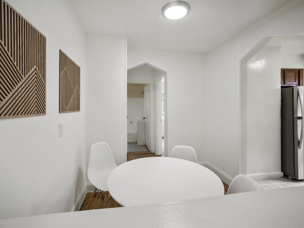A white dining table is surrounded by white chairs in a white room.