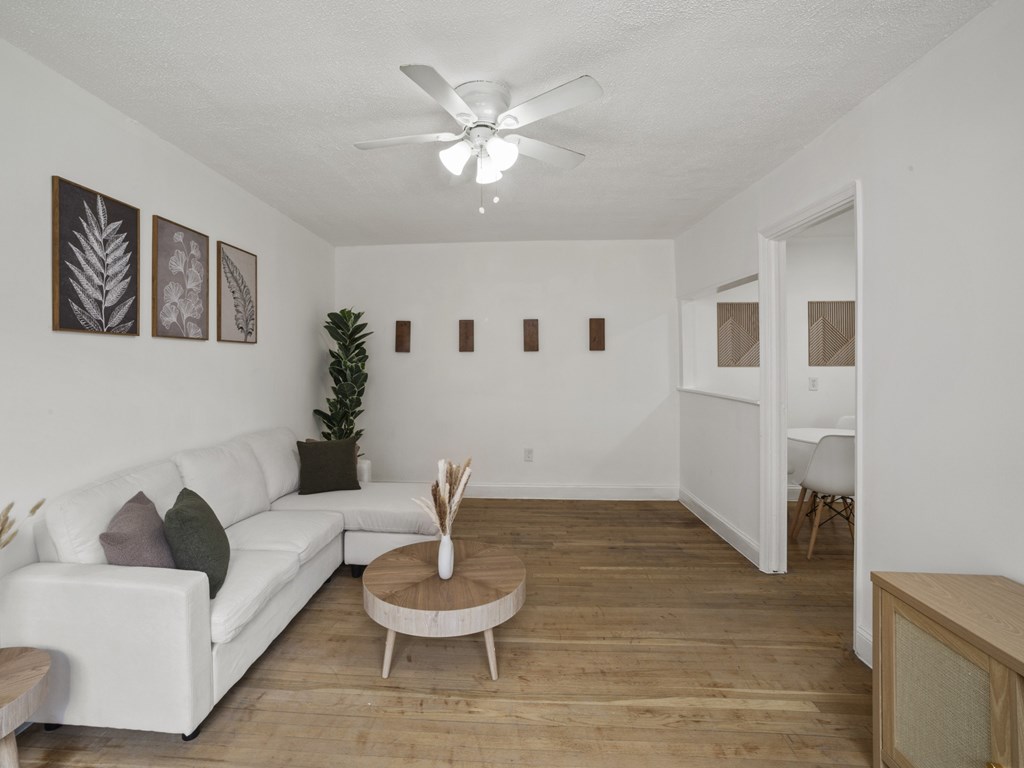 A living room with a white couch, a wooden coffee table, and a ceiling fan.
