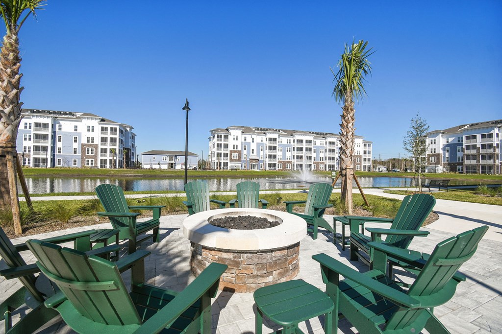 an outdoor patio with chairs and a fire pit with a lake and apartment buildings