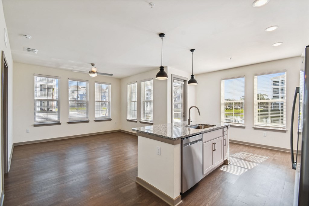 an empty living room with a kitchen with a sink and a window