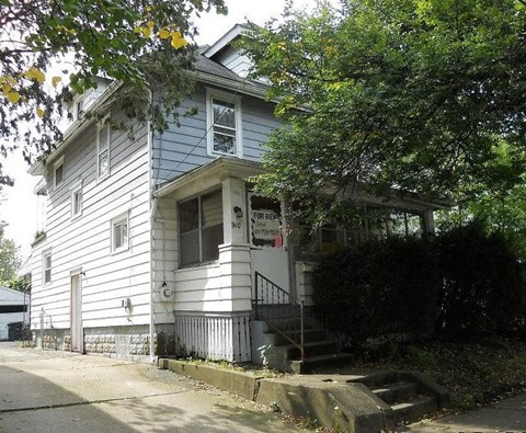 A two-story house with a porch and a tree in front.