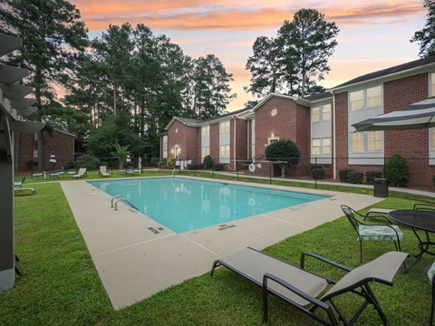 A pool surrounded by lawn chairs and trees.