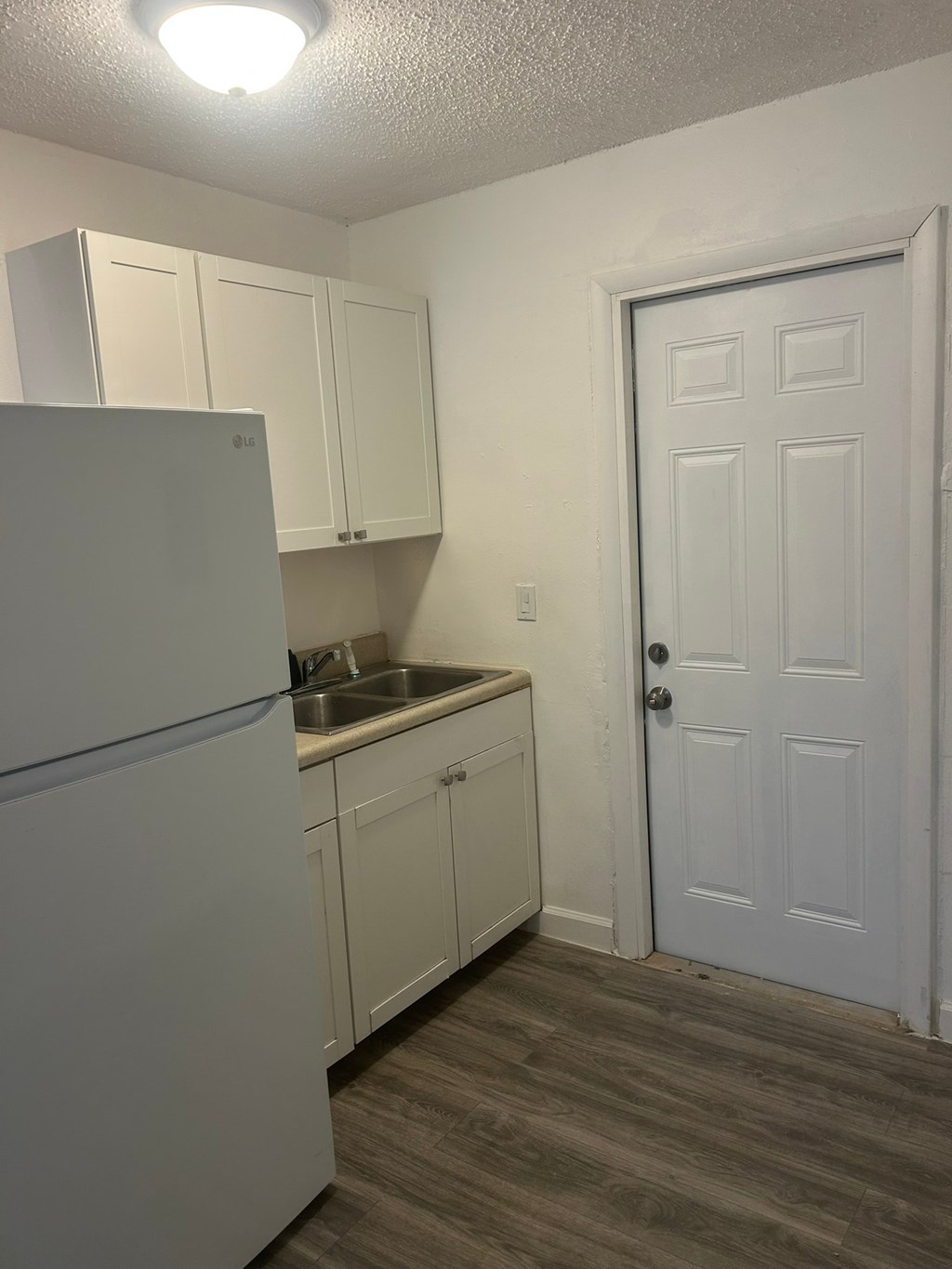 A small kitchen with a white refrigerator and a white door.