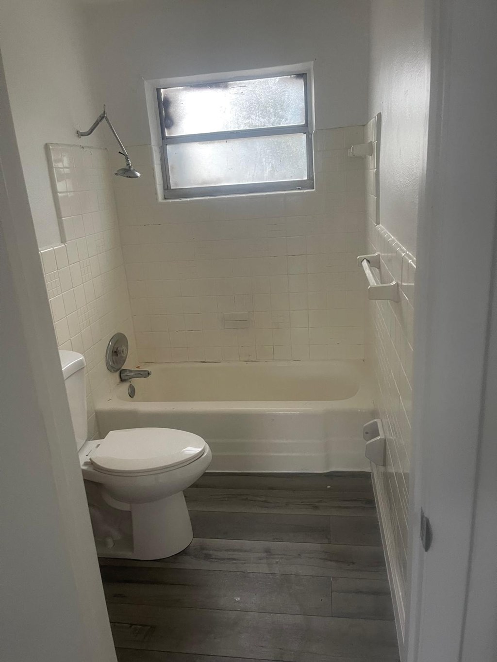 A white toilet in a small bathroom with a window above it.