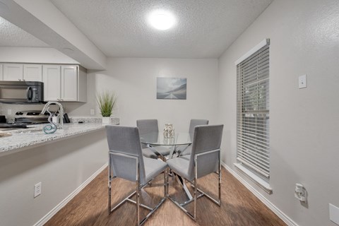 a dining area with a glass table and chairs and a kitchen with a window
