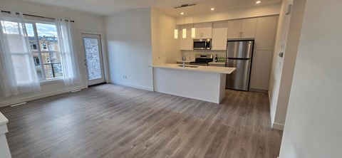 an empty living room with a kitchen and a large window