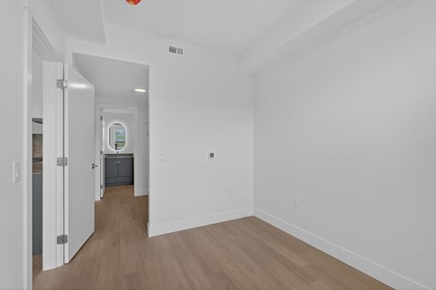 A room with white walls and wooden flooring with a doorway leading to another room.