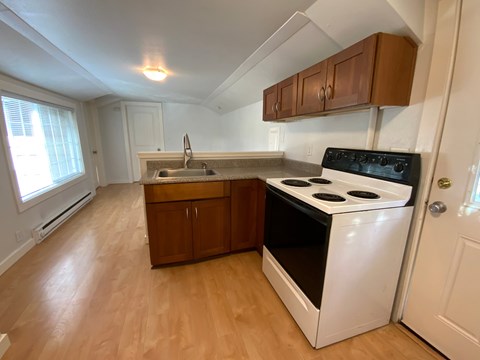 A kitchen with a white stove top oven and wooden floors.
