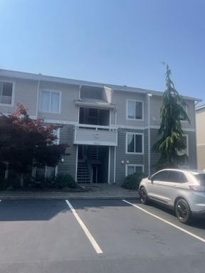 A silver car is parked in front of a grey building.
