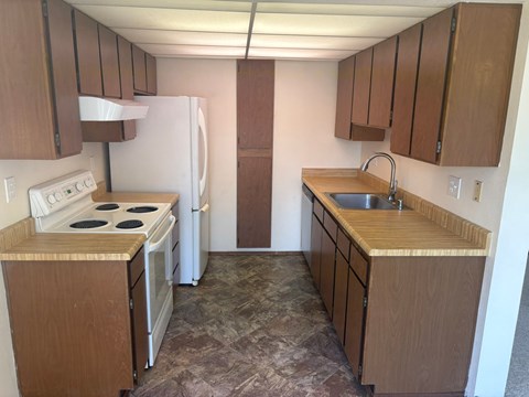 A kitchen with a white refrigerator, wooden cabinets, and a tiled floor.