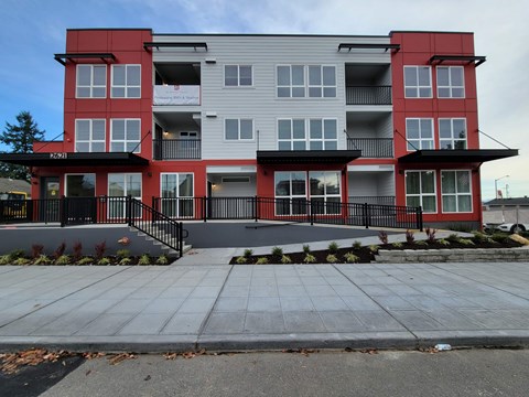 A modern two-story apartment building with red and grey exterior.