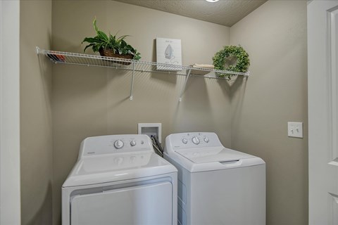 A laundry room with two washing machines and shelves with plants and a wreath.
