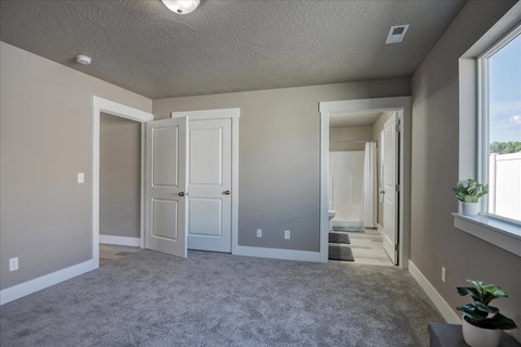 A room with grey carpet and white walls with a door and a window.