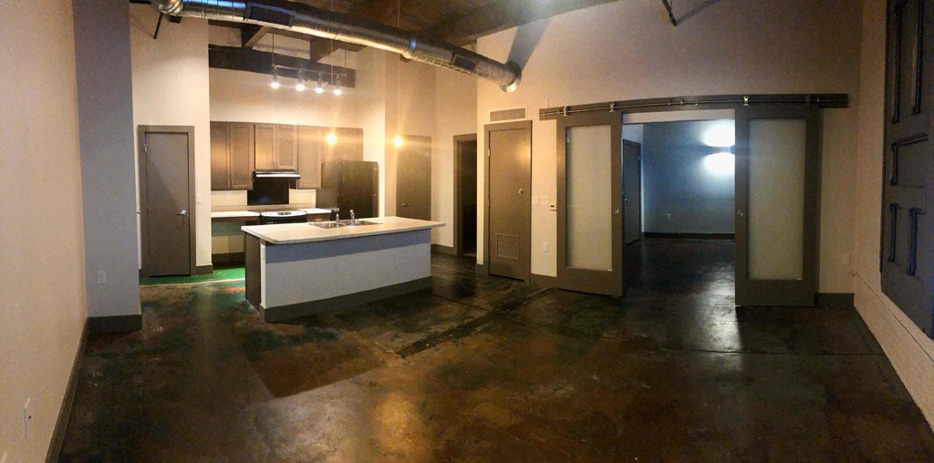 A large empty room with a kitchenette and a refrigerator.