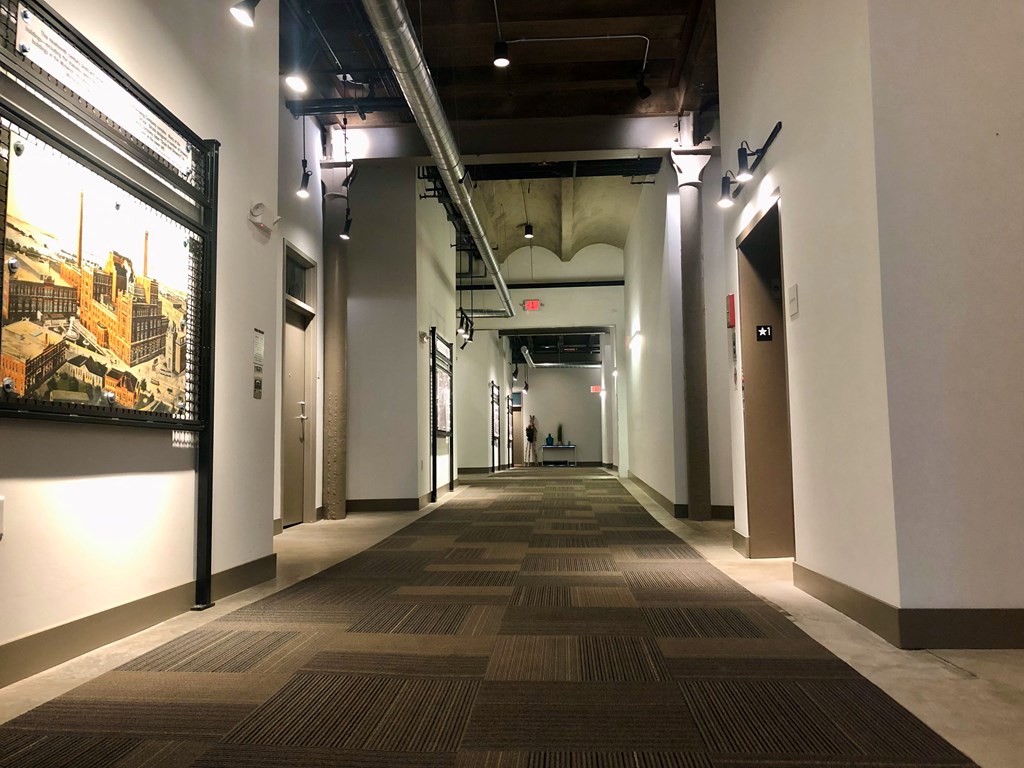 A long hallway with a carpeted floor and a painting on the wall.