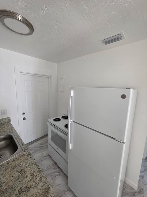 A white fridge and oven in a kitchen with a sink.