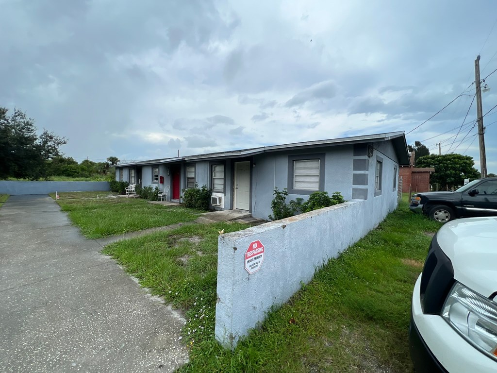 A white car is parked in front of a grey building with a red door.